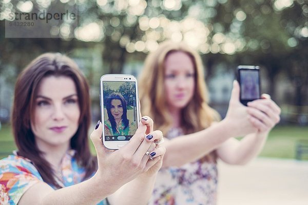 Zwei junge Freundinnen nehmen Selfie auf Smartphones im Einklang