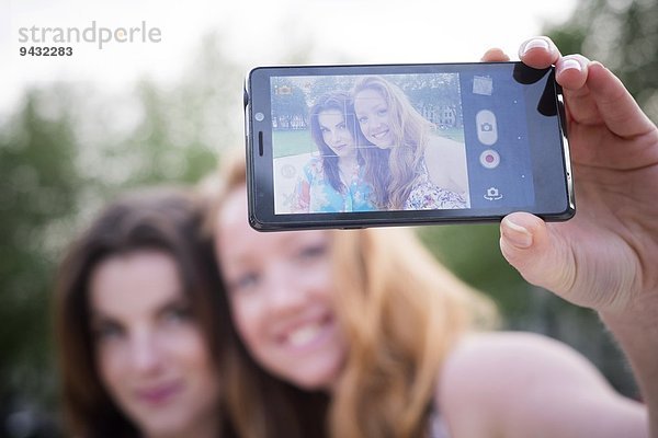 Nahaufnahme von zwei jungen Freundinnen  die Selfie auf dem Smartphone im Park mitnehmen.