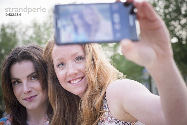 Nahaufnahme von zwei jungen Freundinnen im Park mit Selfie auf dem Smartphone