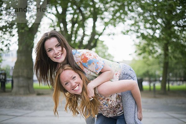 Porträt von zwei jungen Freundinnen  die Huckepack im Park geben