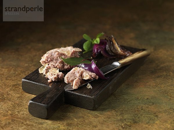 Weihnachtssnack aus Hühner- und Schinkenterrine mit roten Zwiebeln  Lorbeer- und Basilikumblättern auf dem Schneidebrett