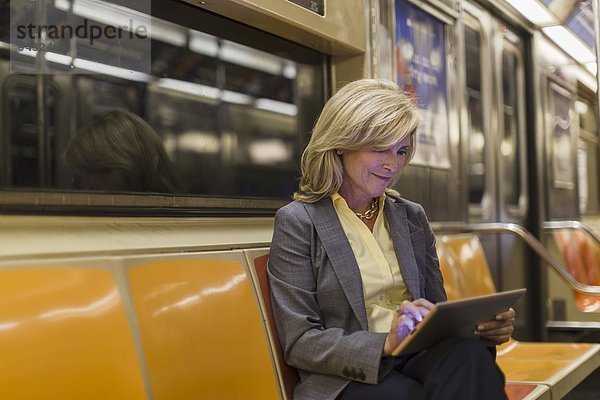 Reife Frau sitzend in der U-Bahn mit digitalem Tablett