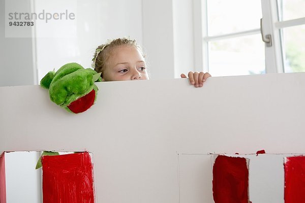 Mädchen blickt über das Spielzeugtheater mit Puppe