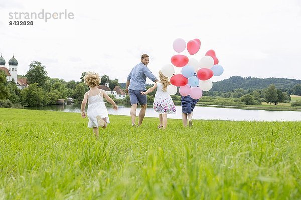 Familie läuft mit Luftballons durchs Feld