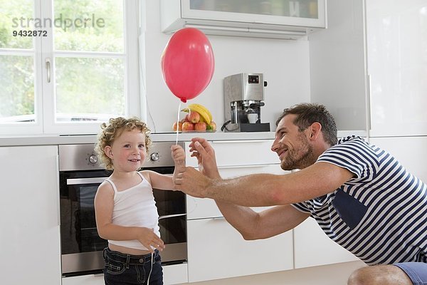 Mädchen hält Ballon mit Vater in der Küche