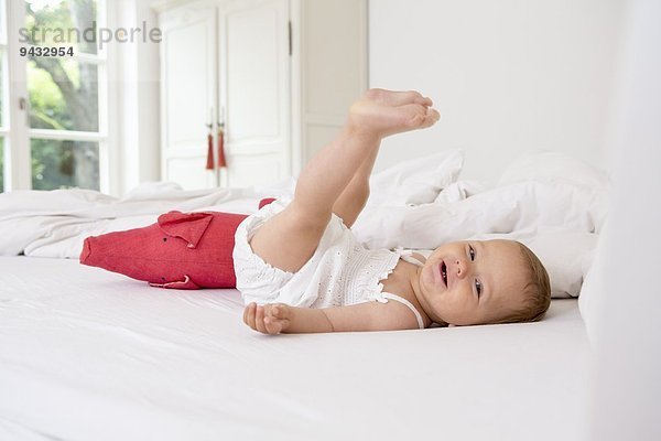 Kleines Mädchen auf dem Bett liegend mit erhobenen Beinen