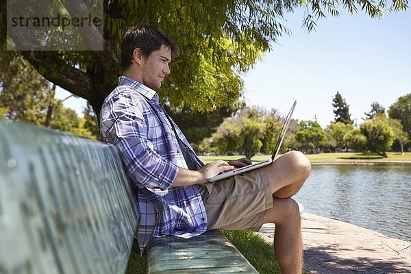 Mann mit Laptop auf Parkbank
