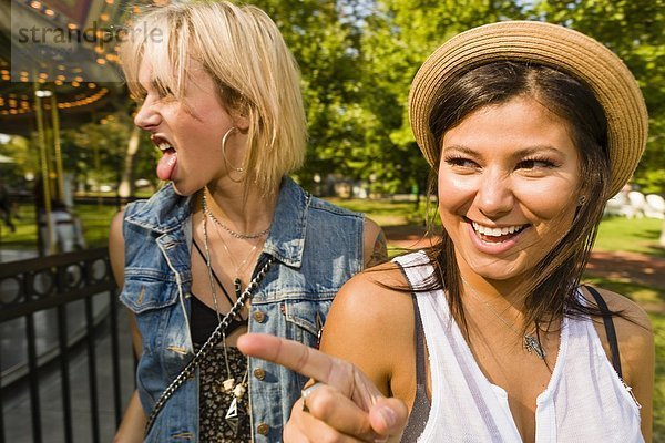 Zwei junge Frauen  die im Park die Zunge zeigen und herausstrecken.