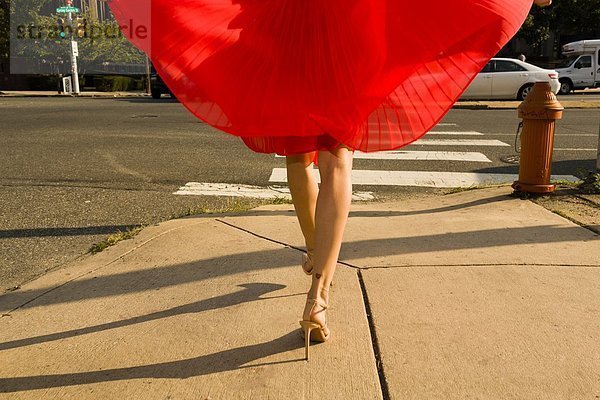 Taille unten Aufnahme einer jungen Frau  die den Bürgersteig entlang schlendert und einen roten Rock trägt.