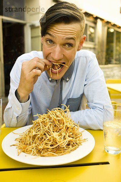 Junger Mann isst dünne Pommes frites im Straßencafé