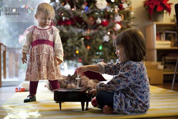 Zwei junge Schwestern  die zu Weihnachten eine Spieluhr mit Spielzeugklavier hören