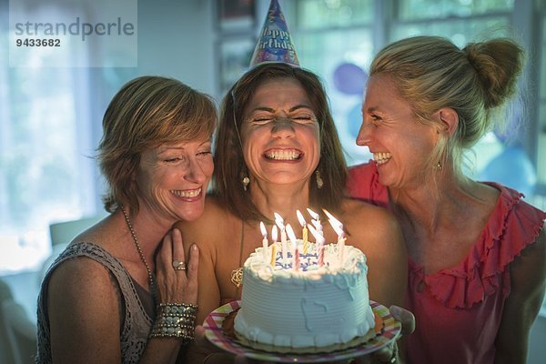 Reife Frau hält Geburtstagskuchen und wünscht sich  während zwei Freunde zuschauen.