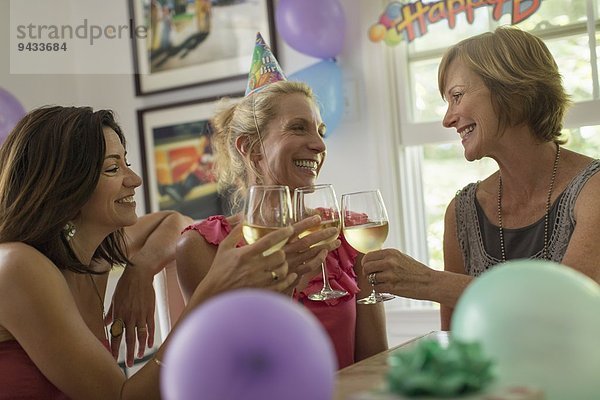 Drei reife Frauen stoßen mit Weingläsern an.