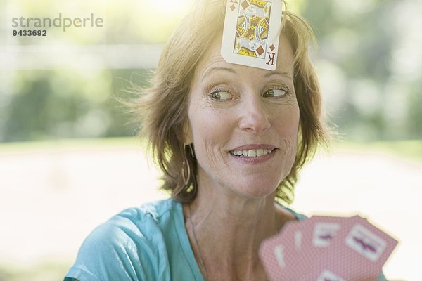 Reife Frau spielt Karten  eine Spielkarte auf die Stirn geklebt