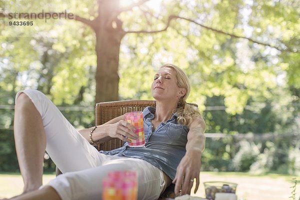 Reife Frau entspannt im Garten mit Getränk