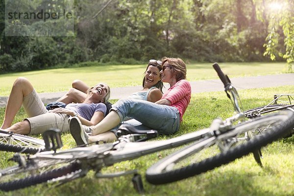 Drei erwachsene Frauen  die sich nach der Fahrradtour auf Rasen entspannen.