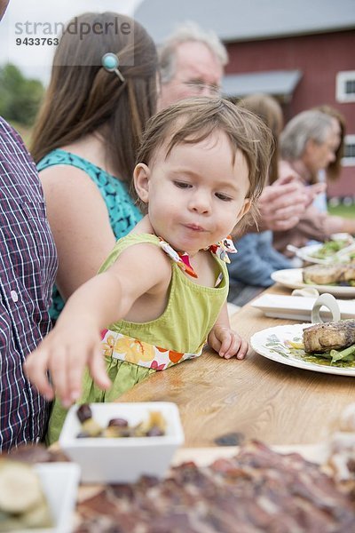 Kleinkind pflückt Oliven vom Teller beim Familienessen  im Freien
