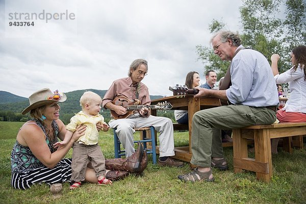 Zwei reife Familienmitglieder  die beim Familienessen im Freien musizieren.