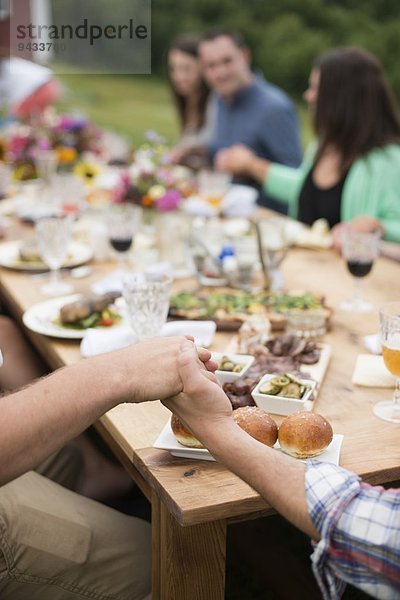 Familie und Freunde halten Händchen am Esstisch  im Freien