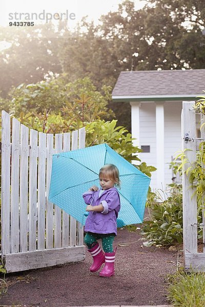 Weibliches Kleinkind beim Spaziergang im Garten mit Regenschirm