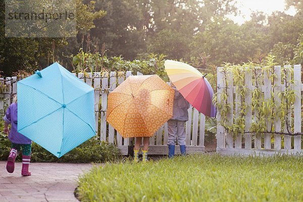 Junge und zwei Schwestern beim Spielen im Garten mit Regenschirmen