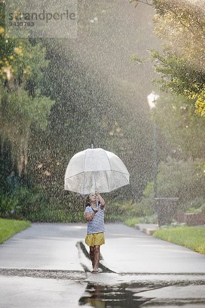 Barfuss-Mädchen hält Regenschirm hoch und läuft durch Pfützen auf der Straße.