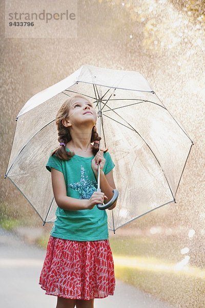 Mädchen hält Regenschirm auf regnerischer Straße hoch