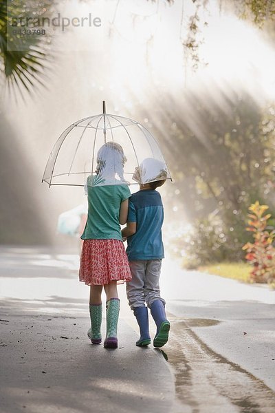 Rückansicht des Jungen und Mädchens mit Regenschirm auf der Straße