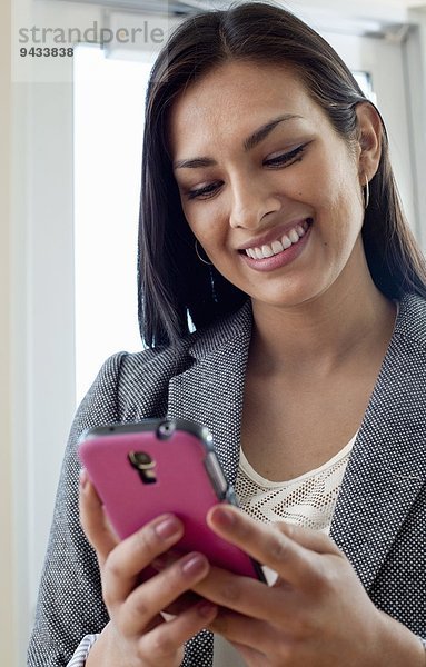 Junge Geschäftsfrau beim Betrachten von Texten auf dem Smartphone im Büro