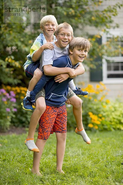 Drei Jungen spielen Huckepack im Garten
