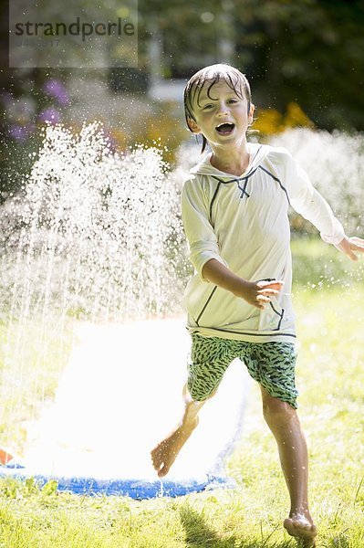 Junge spielt mit Gartensprinkler