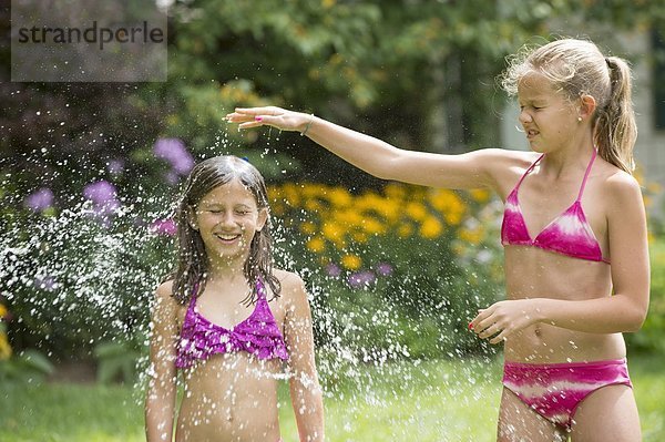 Mädchen in Badeanzug spielen mit Sprinkleranlage