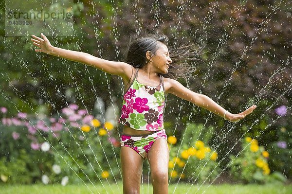 Mädchen in Badeanzug spielend mit Gartensprinkler