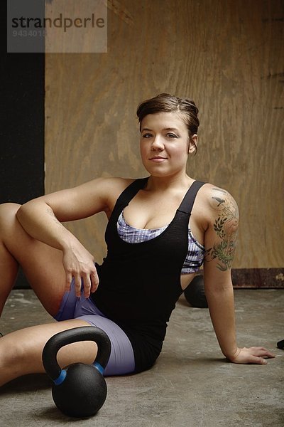 Porträt einer jungen Crossfitterin  die in der Turnhalle auf dem Boden sitzt.