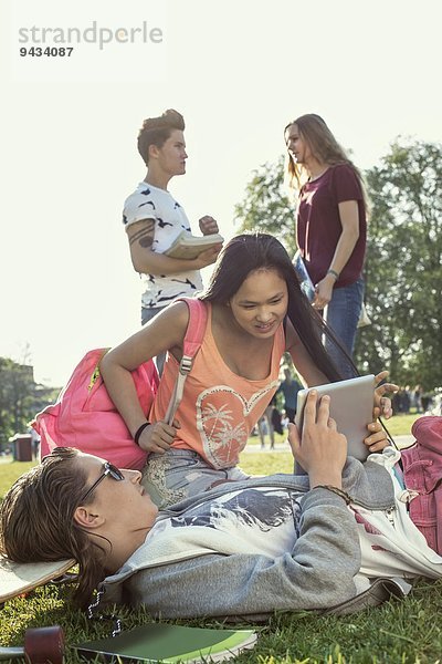 Schüler mit digitalem Tablett auf dem Schulhof mit Freunden  die sich im Hintergrund unterhalten.