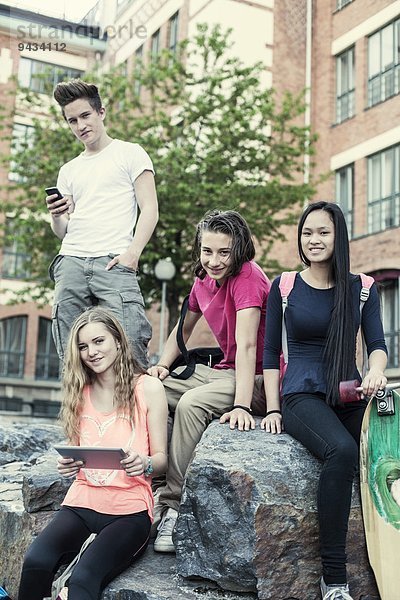 Porträt von lächelnden Gymnasiasten  die auf einem Felsen auf dem Schulhof sitzen.