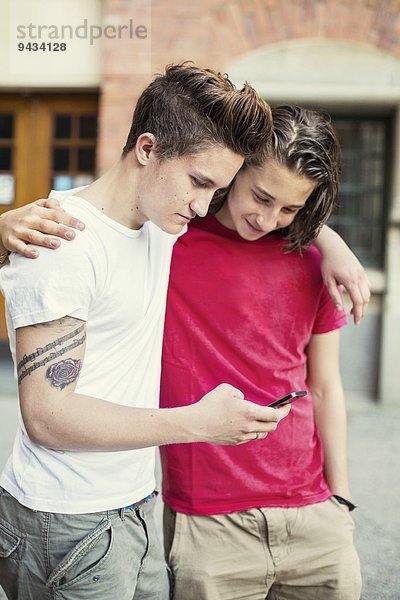 Männliche Freunde lesen SMS auf dem Schulhof auf dem Handy