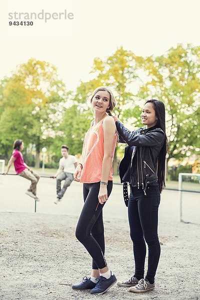 Volle Länge des Gymnasiasten  der die Haare eines Freundes auf dem Schulhof geflochten hat.