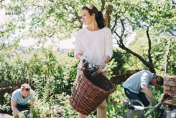 Frau mit Weidenkorb und Männer im Garten im Hintergrund auf dem Hof