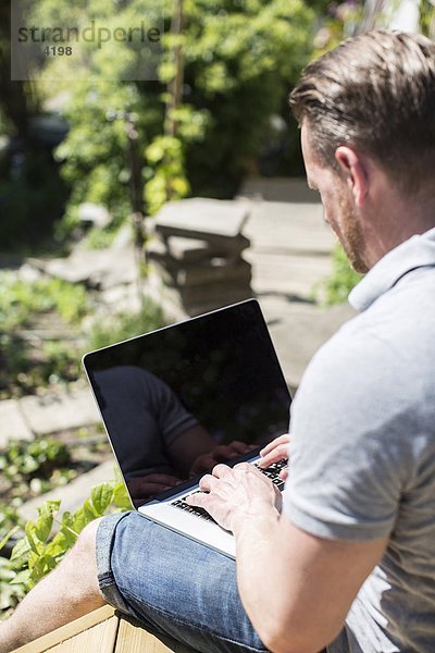 Seitenansicht des Mannes mit Laptop auf der Terrasse