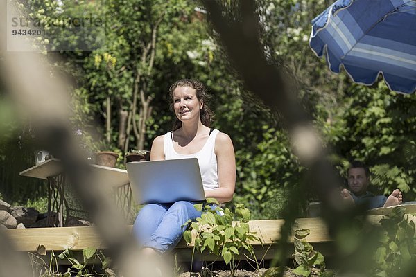 Lächelnde mittlere erwachsene Frau mit Laptop auf der Terrasse sitzend