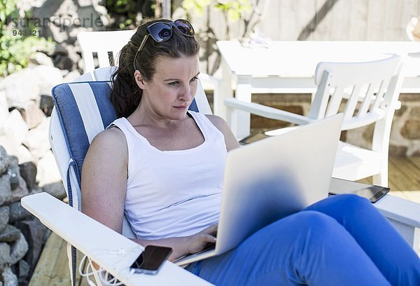 Mittlere erwachsene Frau mit Laptop auf dem Sessel im Hof