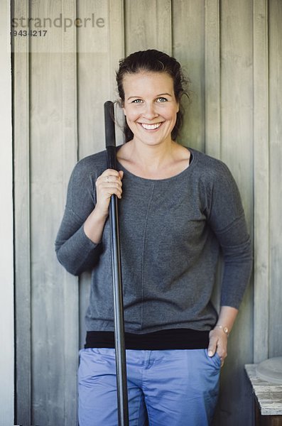 Porträt einer glücklichen Frau  die eine Schaufel hält  während sie an der Wand steht.