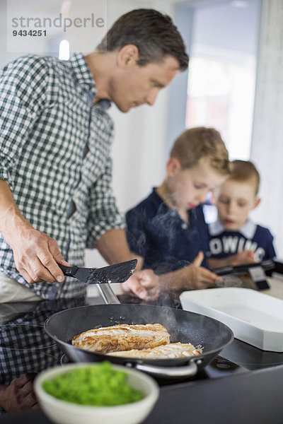 Vater sieht sich Söhne mit digitalen Tabletten an  während sie in der Küche Essen zubereiten.
