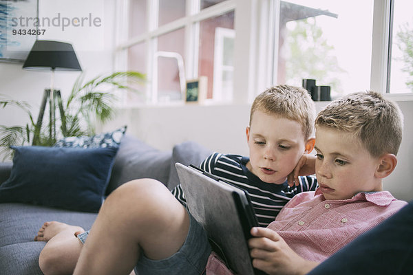 Brüder  die zu Hause ein digitales Tablett auf dem Sofa benutzen
