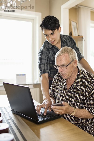 Enkel unterstützt Großvater bei der Nutzung des Laptops zu Hause