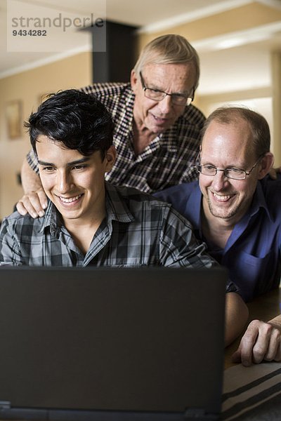 Fröhliche Drei-Generationen-Familie mit Laptop zusammen im Haus