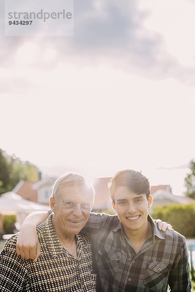 Porträt eines glücklichen Großvaters und Enkels mit Armen gegen den Himmel
