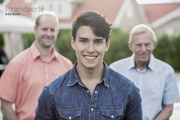 Porträt eines selbstbewussten jungen Mannes mit Großvater und Vater im Hof stehend