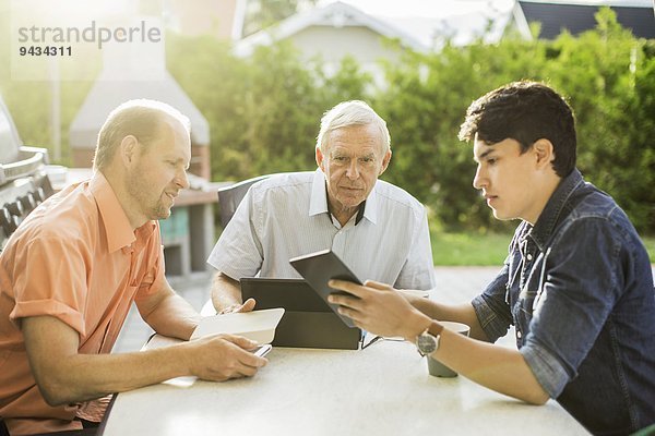 Drei Generationen von Männern  die Technologien bei Tisch auf dem Hof verwenden.